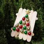 An ornament made out of wooden popsicle sticks that hold 15 mini ball ornaments placed together to make the shape of a Christmas tree.